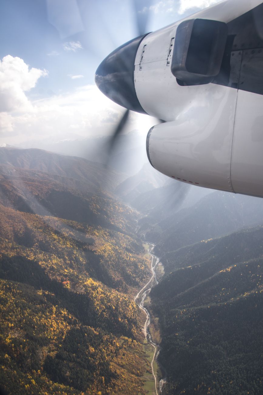 white airplane flying over green and brown mountains